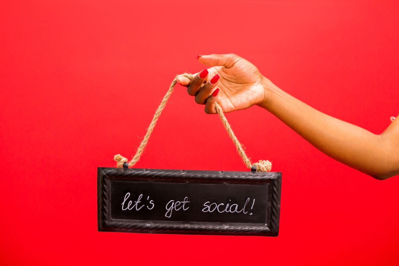 A hand holding a Lets Get Social! sign against a vibrant red background, perfect for online engagement themes.